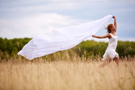Image of happy woman with white fabric running down meadow